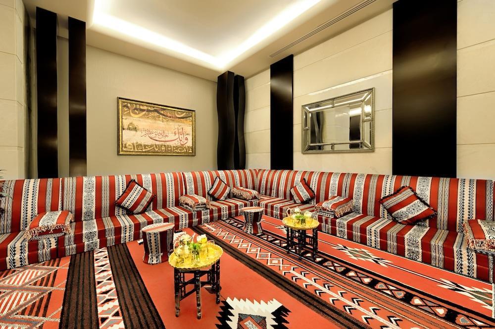 Al Ghufran Safwah Hotel Makkah Mekka Buitenkant foto The photo depicts a spacious and elegantly designed living room. The seating area features a large, L-shaped couch adorned with colorful cushions, primarily in red, black, and white patterns. The walls are decorated with sleek, modern finishes, and l