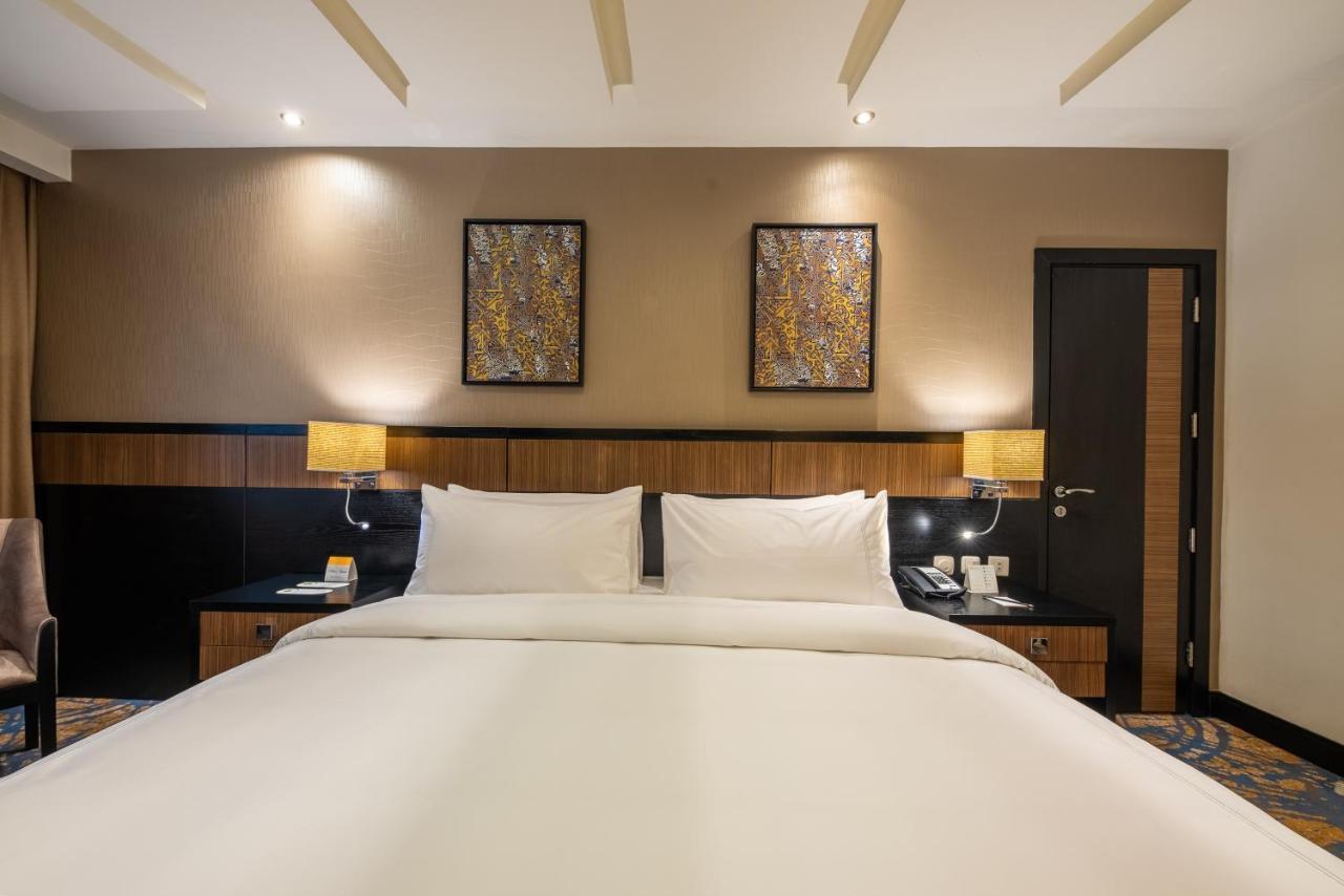 Al Ghufran Safwah Hotel Makkah Mekka Buitenkant foto The photo shows a hotel room featuring a large bed with white linens and two pillows. The background includes wooden elements, with bedside lamps on either side of the bed. Above the bed, there are two decorative wall art pieces. A dark-colored door 