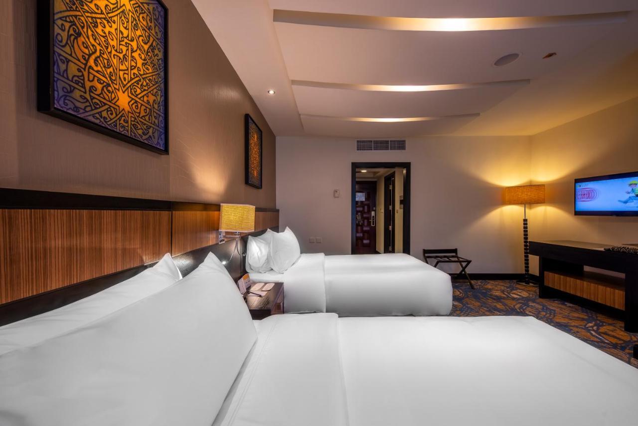 Al Ghufran Safwah Hotel Makkah Mekka Buitenkant foto The photo shows a modern hotel room featuring two beds with white linens placed side by side. There are decorative elements on the walls, including artworks that appear to be framed and feature intricate designs. The room has ambient lighting, with a