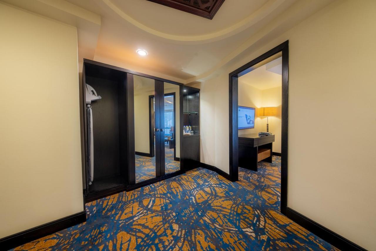 Al Ghufran Safwah Hotel Makkah Mekka Buitenkant foto The photo shows the interior of a hotel room. There is a small entryway with a patterned carpet featuring blue and yellow colors. On one side, there is a closet with mirrored doors. Opening into the room, there are two doorways: one leads to a bathro