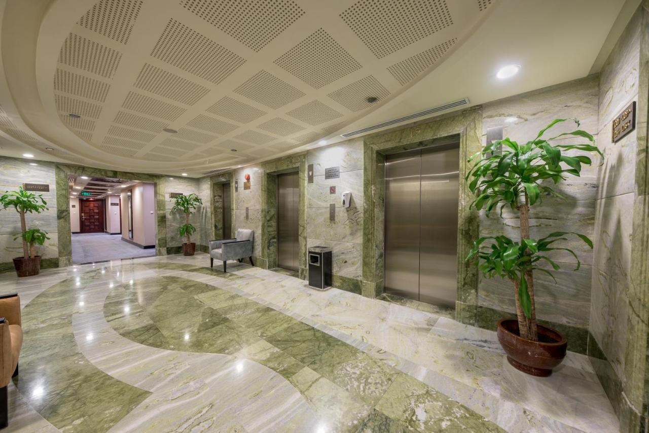 Al Ghufran Safwah Hotel Makkah Mekka Buitenkant foto The photo depicts a spacious lobby area, likely in a building or hotel. The floor is made of polished marble with a flowing pattern, and the walls are lined with light-colored marble. 

There are two elevator doors visible, and next to them is a smal