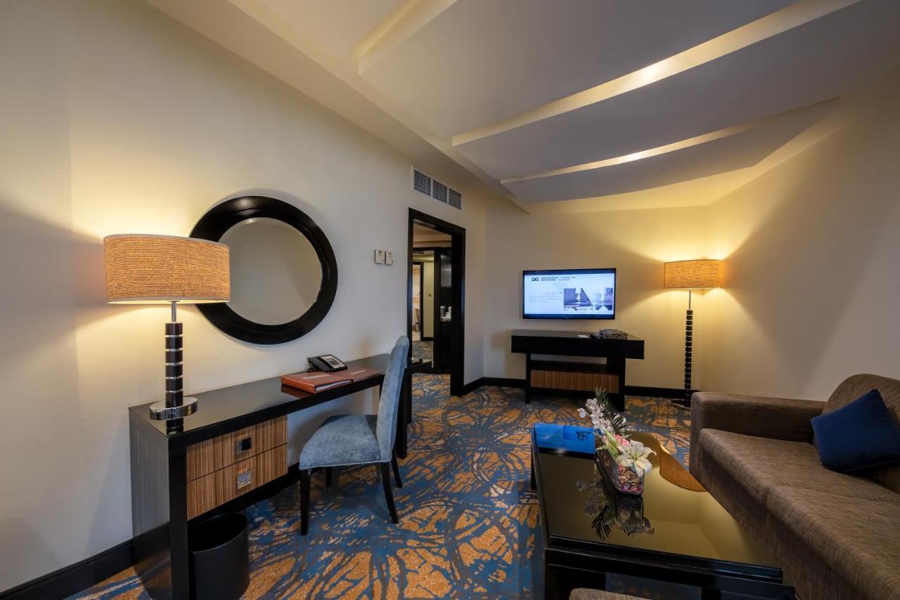 Al Ghufran Safwah Hotel Makkah Mekka Buitenkant foto The image shows a hotel room or a similar space designed for relaxation and comfort. It features a stylish desk with a lamp, a comfortable chair, and a large mirror mounted on the wall. There is a television mounted on the wall or sitting on a cabine