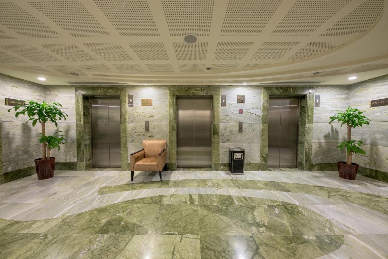 Al Ghufran Safwah Hotel Makkah Mekka Buitenkant foto The image shows a lobby area with a modern design. It features several elevator doors arranged in a row. The walls are made of a light-colored marble with a green hue, and the flooring is also marble, creating a cohesive and elegant look. On either s