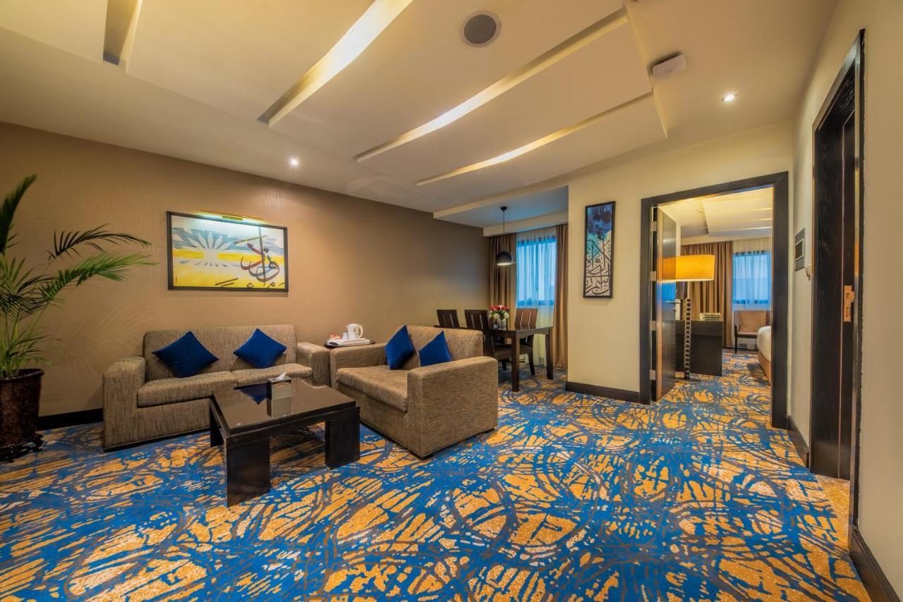 Al Ghufran Safwah Hotel Makkah Mekka Buitenkant foto The photo shows a modern and well-decorated living area, likely in a hotel suite or a well-appointed home. 

- **Furniture**: There are two light-colored sofas with blue cushions, arranged around a dark coffee table. 
- **Artwork**: On the wall, ther
