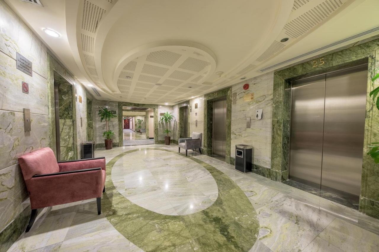 Al Ghufran Safwah Hotel Makkah Mekka Buitenkant foto The photo shows a well-appointed hallway in a building, likely a hotel or office space. The walls are decorated with a light marble finish, and there are green marble accents. The floor features a circular design in light and dark colors, adding a to