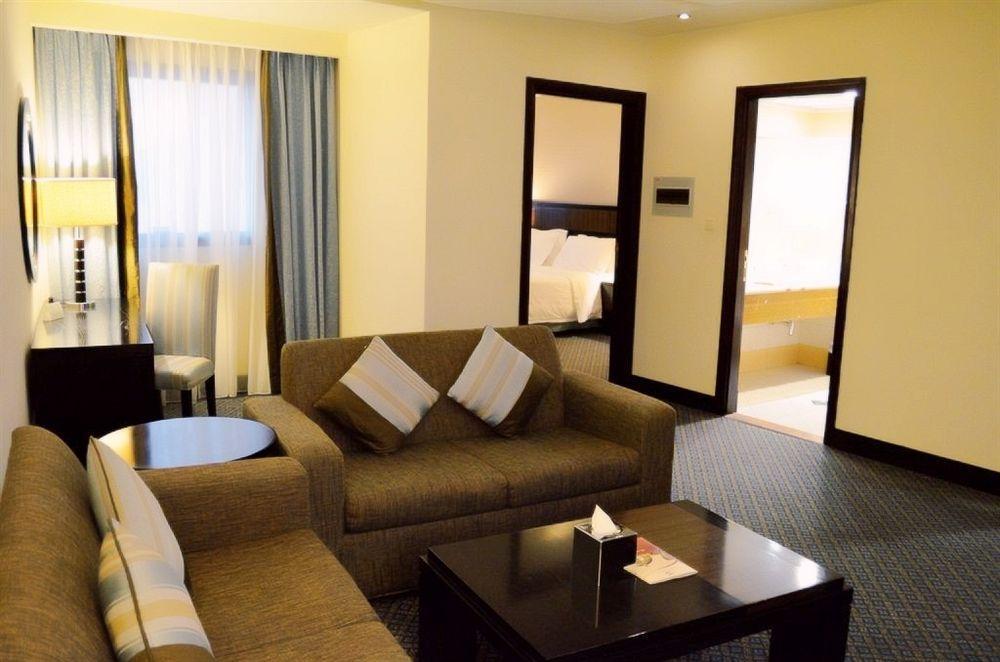 Al Ghufran Safwah Hotel Makkah Mekka Buitenkant foto The photo shows a hotel suite or living area. It features a comfortable-looking sofa with decorative pillows, a small round table beside it, and a dark coffee table in front. Light streams in from large windows covered with curtains, creating a brigh