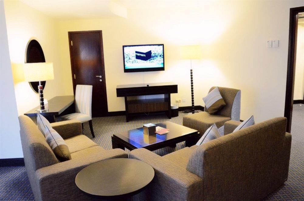 Al Ghufran Safwah Hotel Makkah Mekka Buitenkant foto The photo shows an indoor living area that appears to be a modern hotel suite. The space features two armchairs and a sofa arranged around a coffee table. A flat-screen television is mounted on the wall opposite the seating area. There is a small rou