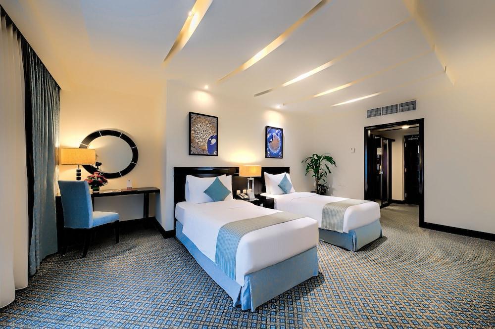 Al Ghufran Safwah Hotel Makkah Mekka Buitenkant foto The photo shows a modern hotel room featuring two single beds with light blue accents. There is a decorative piece of artwork on the wall above each bed. A round mirror is also hanging on the wall, complemented by a stylish lamp on a wooden bedside t