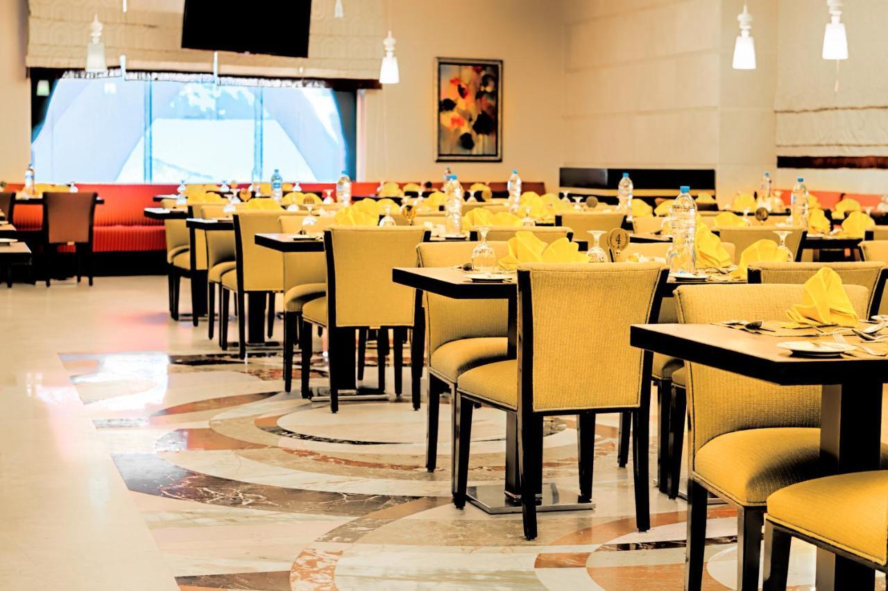 Al Ghufran Safwah Hotel Makkah Mekka Buitenkant foto The photo features a dining area with several tables and chairs arranged neatly. The chairs have yellow upholstery, and each table is set with yellow napkins. The flooring has a marble design, and there are decorative elements in the background, incl