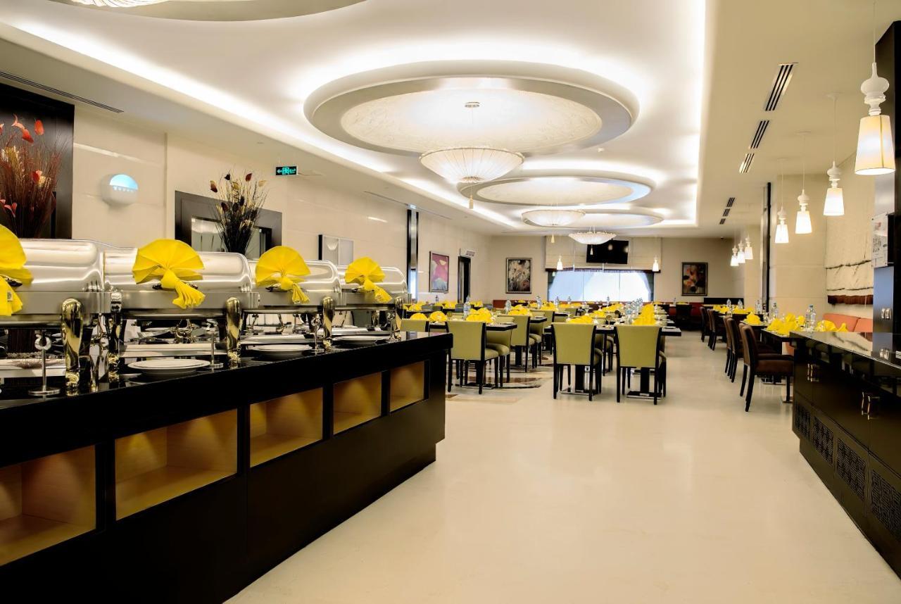 Al Ghufran Safwah Hotel Makkah Mekka Buitenkant foto The photo depicts a modern restaurant interior. There is a wide open space with a contemporary design. On one side, there are several buffet-style food trays, likely for self-service dining. The tables are set with yellow napkins, and the seating app