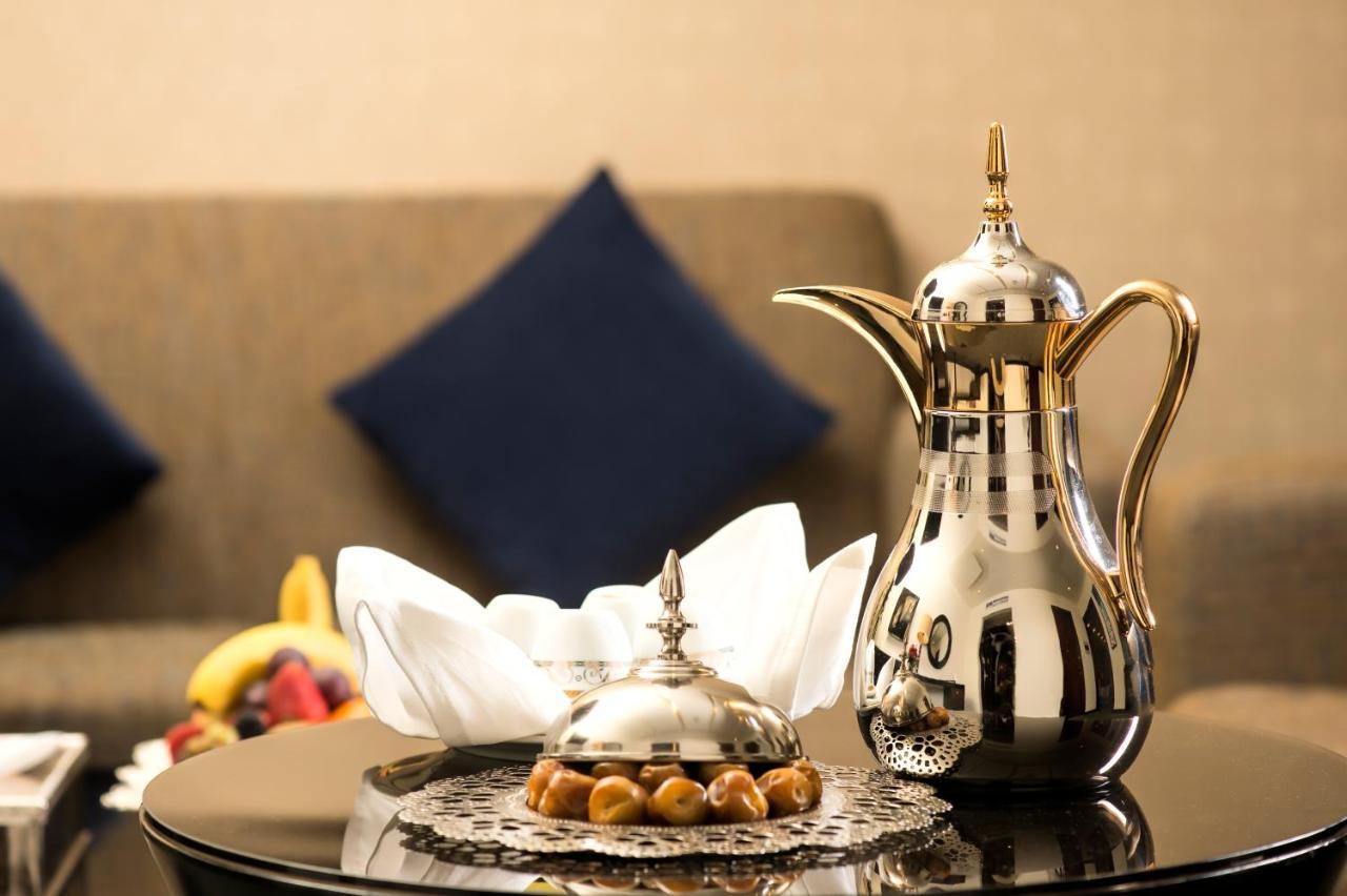 Al Ghufran Safwah Hotel Makkah Mekka Buitenkant foto The photo features a beautifully arranged setting. There is a shiny, ornate coffee pot made of metal, often associated with traditional Arabic coffee. Next to it is a decorative dish, also metallic, likely used for serving sweets or snacks. The dish 