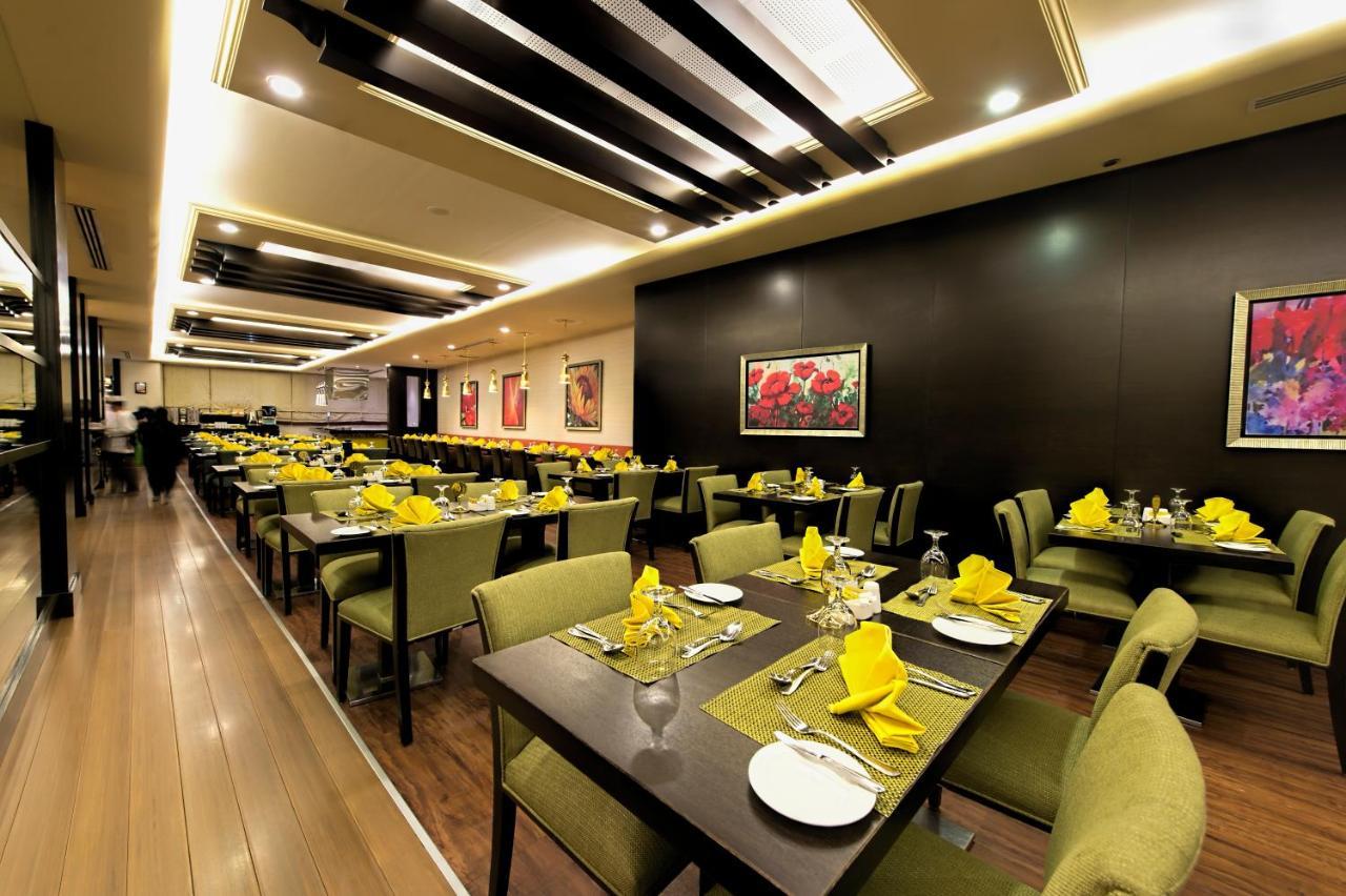 Al Ghufran Safwah Hotel Makkah Mekka Buitenkant foto The photo shows a modern restaurant interior. It features well-arranged tables with green chairs and yellow napkins. Each table is set with glassware and utensils, suggesting a dining setup for guests. The walls have artwork, and the lighting is warm