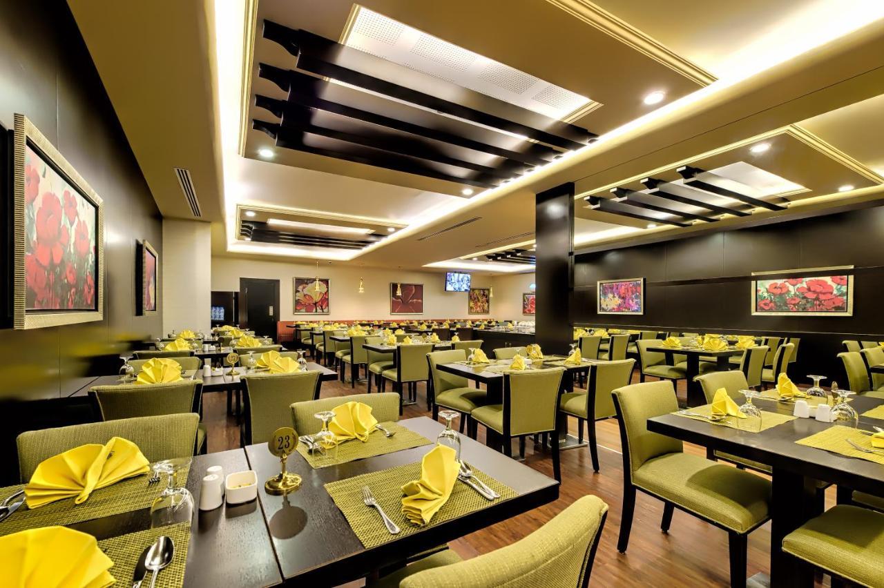 Al Ghufran Safwah Hotel Makkah Mekka Buitenkant foto The photo shows a modern restaurant interior. The space features neatly arranged tables with green chairs, and each table is set with yellow napkins, cutlery, and glasses. The lighting is warm and inviting, with stylish ceiling designs. The walls are