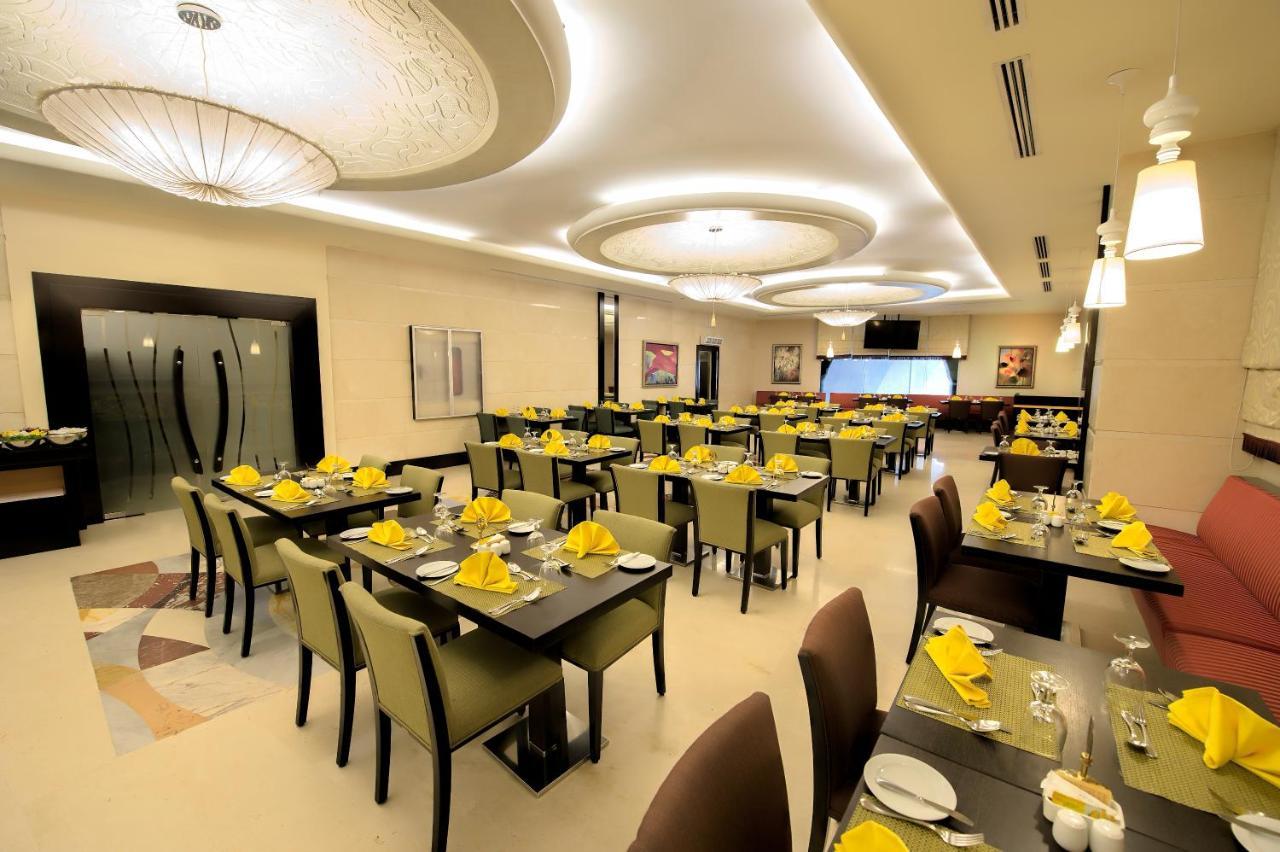 Al Ghufran Safwah Hotel Makkah Mekka Buitenkant foto The photo shows the interior of a modern restaurant. The space features neatly arranged tables with dark wooden surfaces and green chairs. Each table is set with yellow napkins, silverware, and glassware, suggesting a prepared dining atmosphere. The 