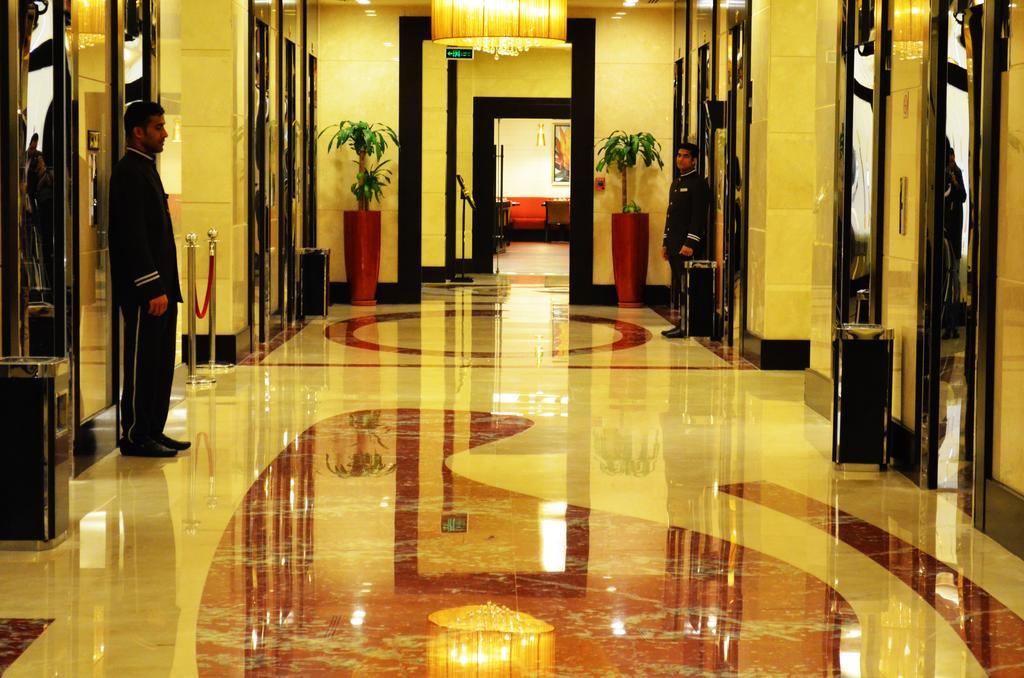 Al Ghufran Safwah Hotel Makkah Mekka Buitenkant foto The photo shows an elegant hallway in a building, likely a hotel or a high-end establishment. The floor is made of polished marble with a decorative pattern. There are two doormen or attendants standing on either side of the hallway, each dressed in 