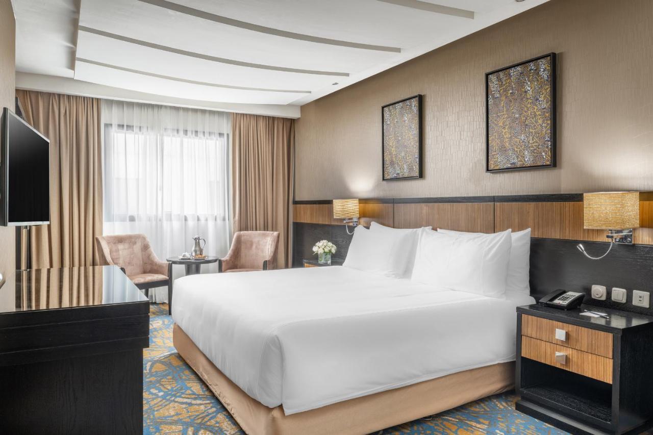 Al Ghufran Safwah Hotel Makkah Mekka Buitenkant foto The photo shows a modern hotel room featuring a spacious layout. In the center, there is a large bed with white linens. To the side, there are two upholstered chairs and a small table, creating a cozy sitting area. The room is decorated with stylish 