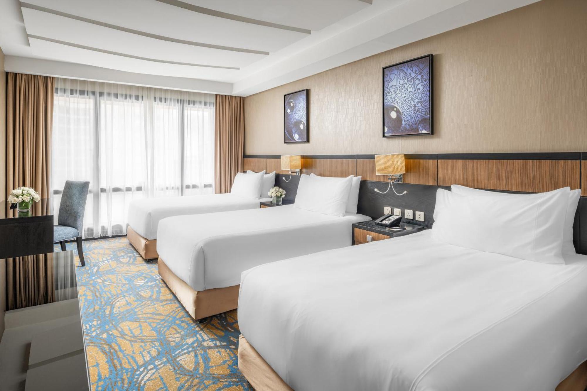 Al Ghufran Safwah Hotel Makkah Mekka Buitenkant foto The photo shows a hotel room featuring three neatly made beds with white linens. The room has a modern and bright design, with large windows allowing natural light to enter. There are two framed artworks on the wall above the beds, contributing to th