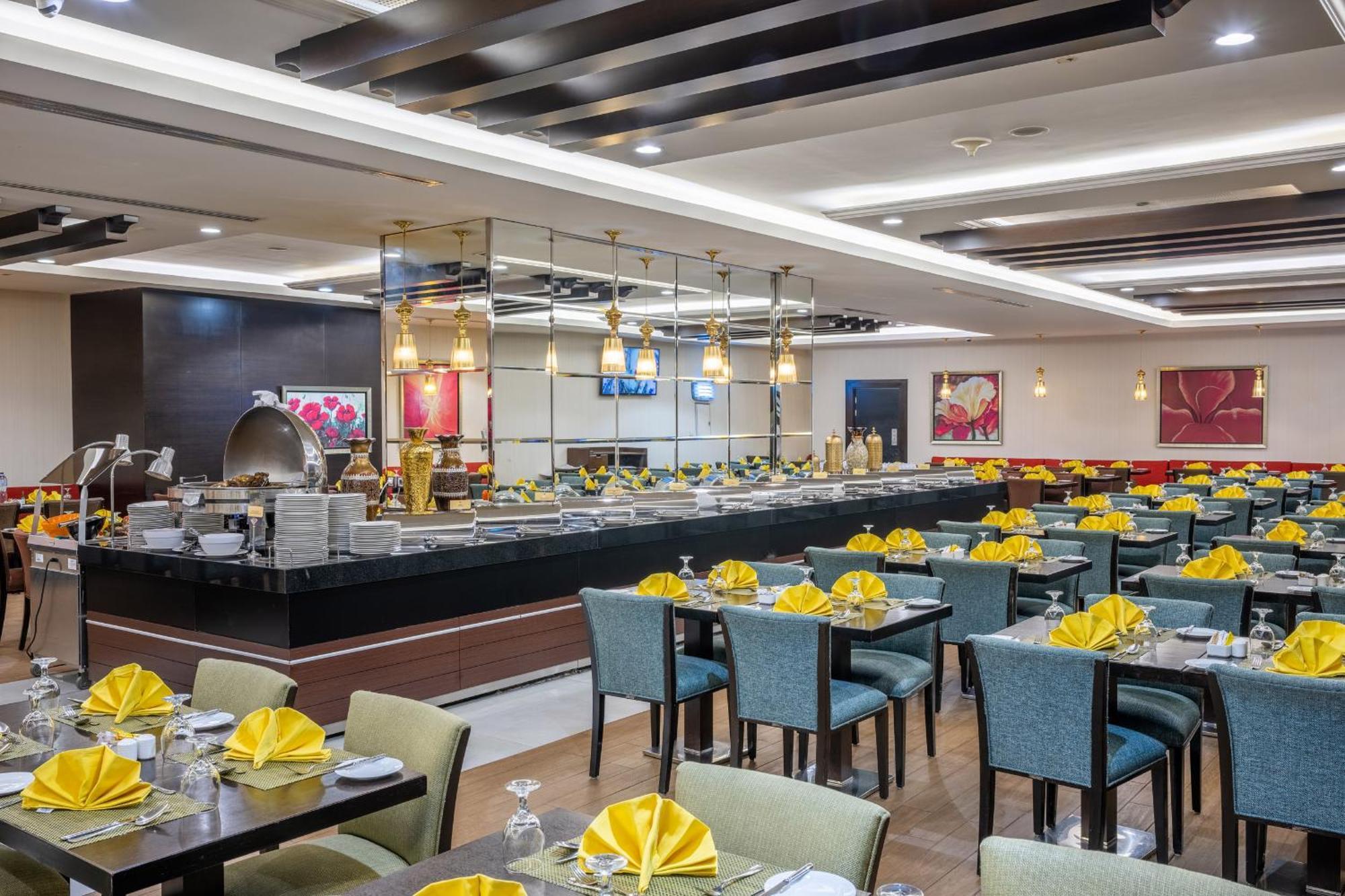 Al Ghufran Safwah Hotel Makkah Mekka Buitenkant foto The photo shows a spacious restaurant interior. There are neatly arranged tables with blue chairs, each set with yellow napkins and silverware. In the background, there's a buffet area with an open layout featuring various food displays. The decor ap