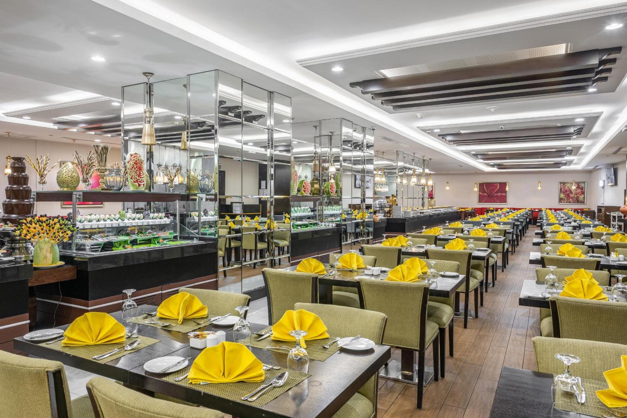 Al Ghufran Safwah Hotel Makkah Mekka Buitenkant foto The photo shows the interior of a restaurant. The space features neatly arranged tables, each covered with a dark tablecloth. Yellow napkins are elegantly folded at each place setting, and there are crystal glasses on the tables. In the background, t