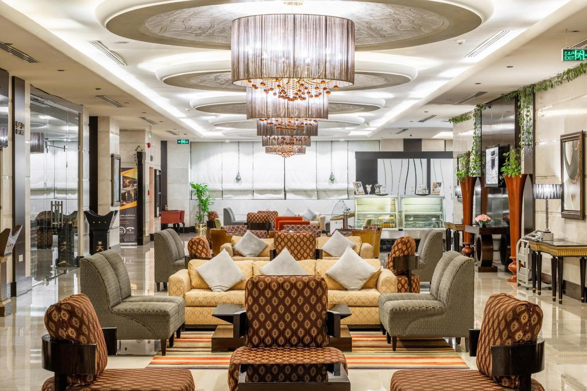 Al Ghufran Safwah Hotel Makkah Mekka Buitenkant foto The photo shows an elegantly designed interior space, likely a hotel lobby or lounge area. It features a combination of stylish seating arrangements, including sofas and armchairs, upholstered in rich fabrics with decorative patterns. The ceiling is 