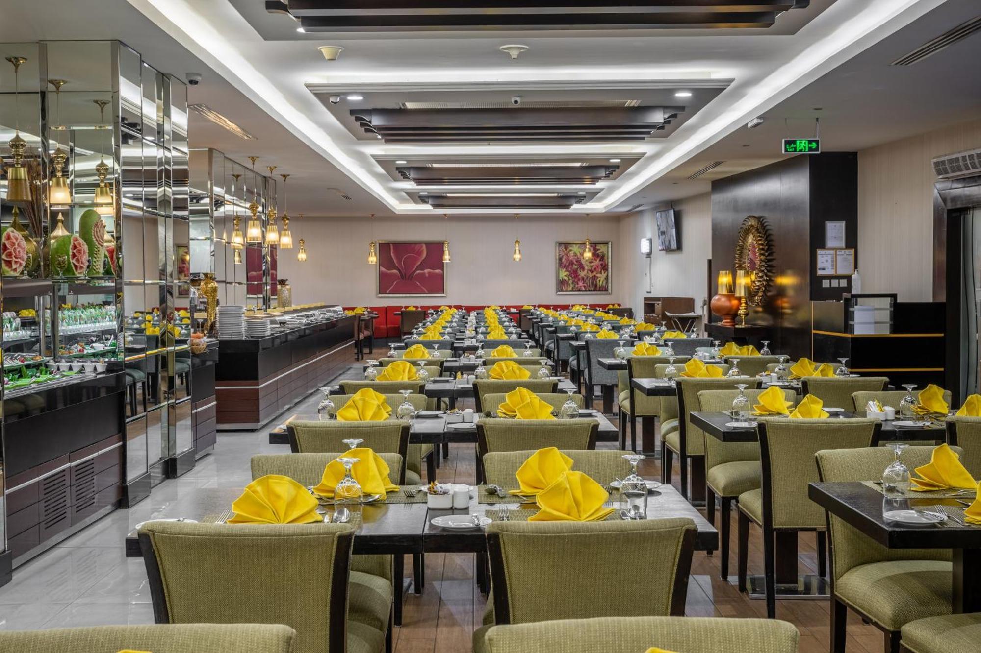 Al Ghufran Safwah Hotel Makkah Mekka Buitenkant foto The photo shows the interior of a restaurant. The dining area features multiple rows of tables, each set with yellow napkins and glassware. The tables are covered with dark-colored tablecloths and are surrounded by green upholstered chairs. The resta