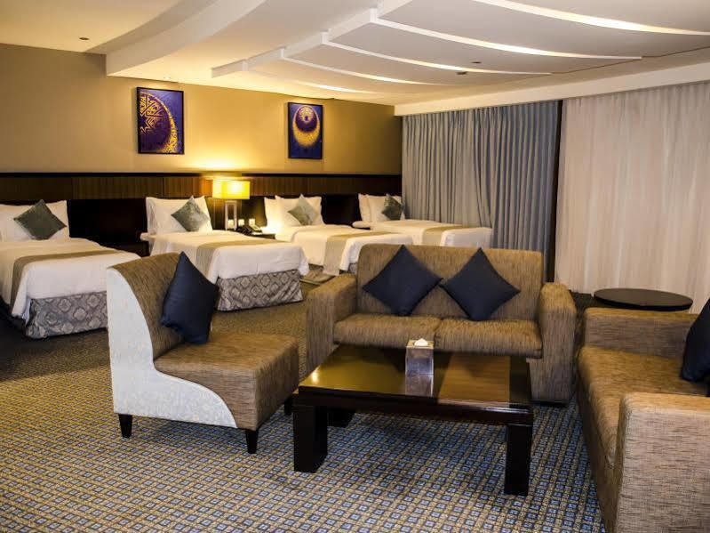 Al Ghufran Safwah Hotel Makkah Mekka Buitenkant foto The photo shows a spacious hotel room that features two large beds with decorative pillows. There is a sitting area with a modern sofa and a coffee table, complemented by two accent chairs. The room is elegantly decorated, with artwork on the walls a